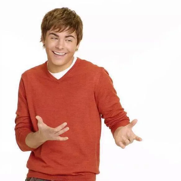 When Your Parents Ask Where All Your Money Went — Zac Efron in an orange sweater laughing with arms spread in a presenting gesture