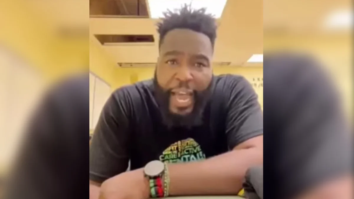 White Man Did It In One Week — Bearded Black man in dark t-shirt speaking to camera while seated at a table