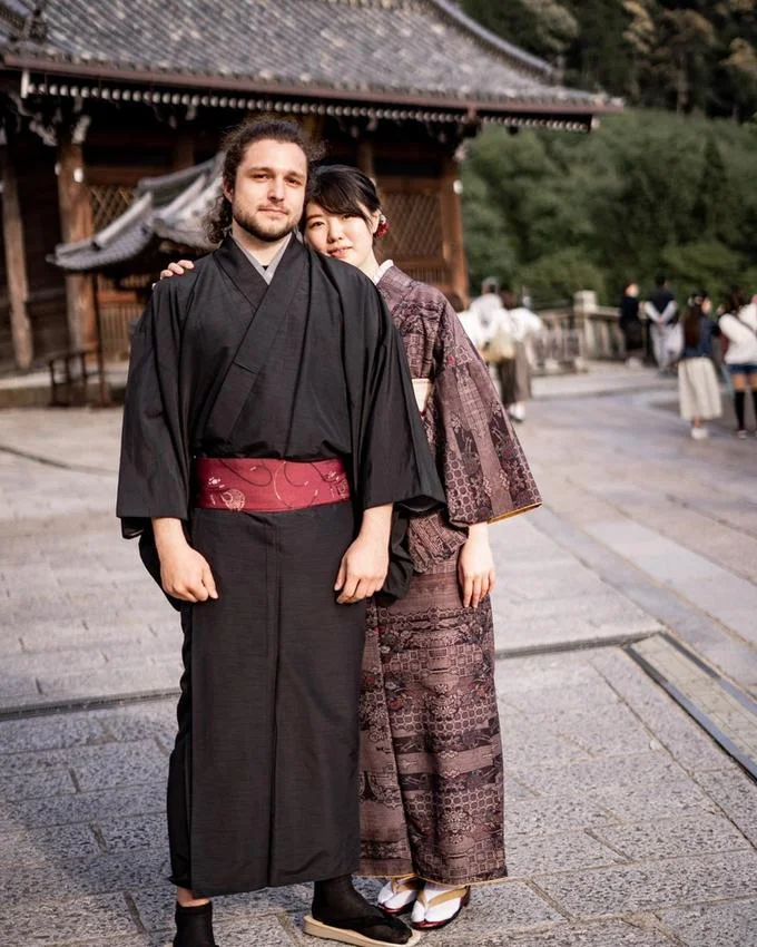 Ken-Sama — Western man in black kimono standing with a Japanese woman in a brown kimono in front of a Japanese temple.