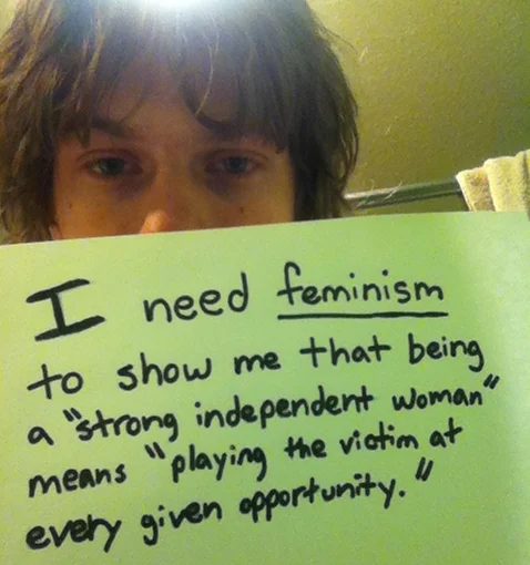 Who Needs Feminism — Man holding handwritten sign expressing parental support for feminism to protect daughters from harassment on campuses.