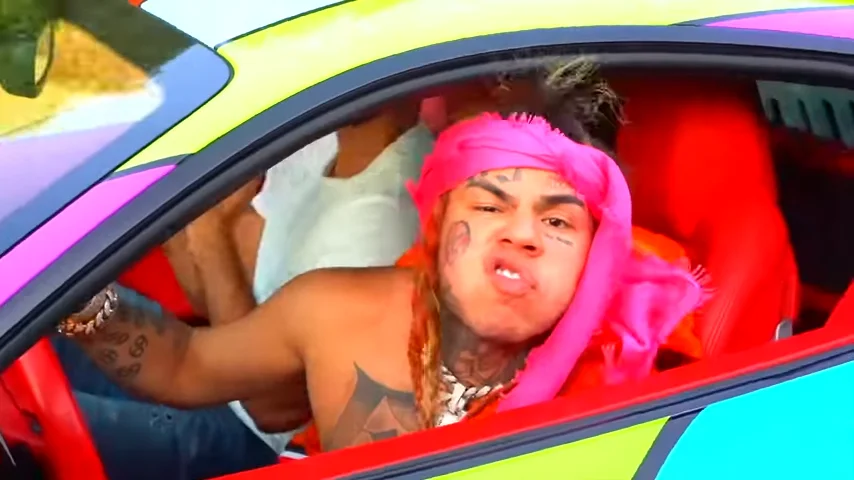 Who the Fuck Is You? — 6ix9ine leaning out of a multicolored car window with pink bandana and rainbow hair