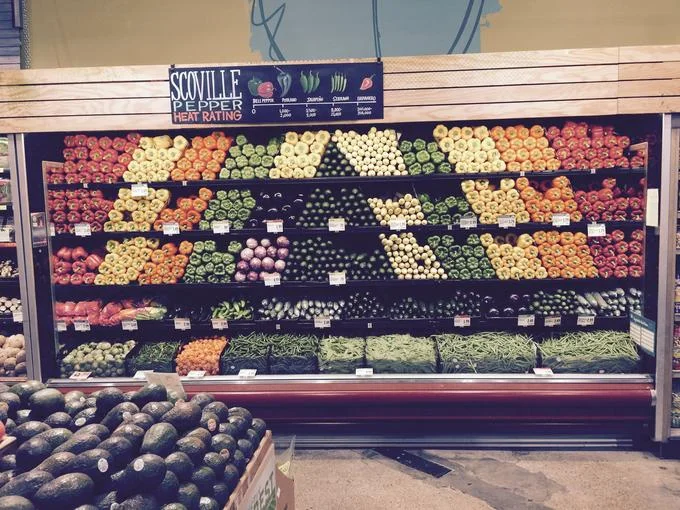 Whole Foods produce aisle with meticulously arranged peppers and a Scoville heat rating sign