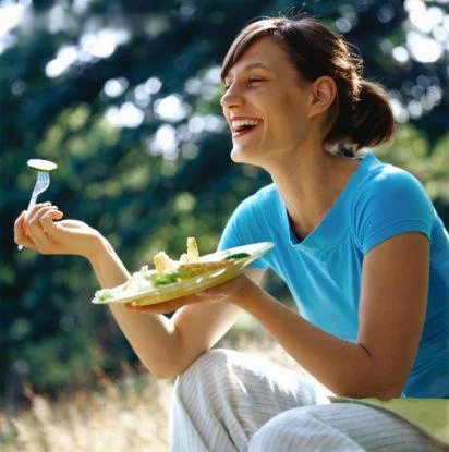 Women Laughing Alone With Salad — Stock photo of brunette woman in blue top laughing exuberantly while eating salad outdoors.