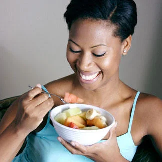 Women Laughing Alone With Salad — Stock photo of Black woman in teal top smiling while eating mixed fruit or light salad.
