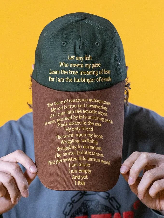 "Women Want Me, Fish Fear Me" Hat Parodies — Person wearing a green cap with a comically extended brown brim covered in a long parody fishing poem.