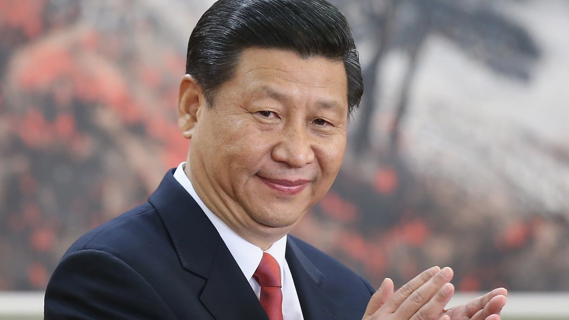 Xi Jinping smiling and clapping in a dark suit with red tie