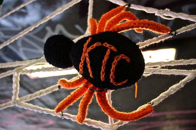 Yarn Bombing — Handcrafted black and orange crocheted spider suspended from white yarn web.