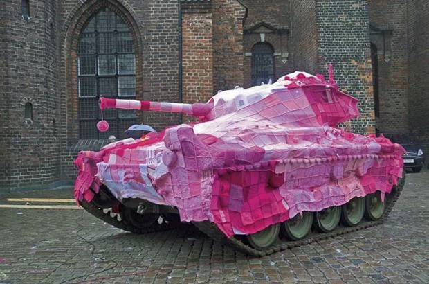 Yarn Bombing — Decommissioned military tank wrapped entirely in pink and mauve knitted and crocheted fabric.