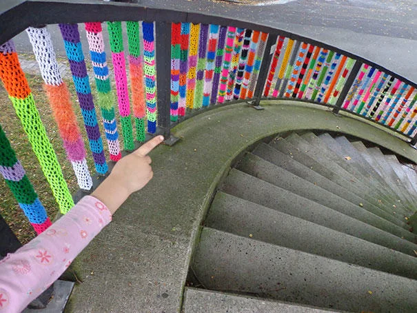 Yarn Bombing — Staircase railing balusters individually wrapped in different bright colored yarn patterns.