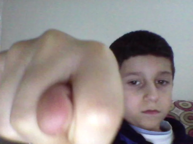 Yotube — Boy extending a fist directly toward the webcam, face partly behind the fist