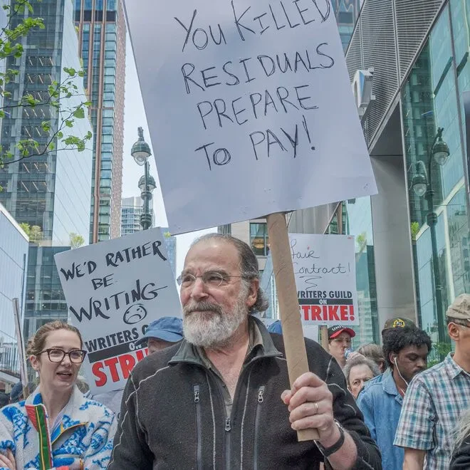 You Killed My Father, Prepare to Die — Mandy Patinkin holding a WGA strike sign reading 'You Killed Residuals Prepare to Pay'