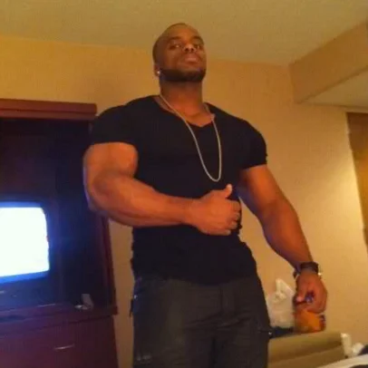 You're In The Club And This Guy Slaps Your Girlfriend's Ass — Muscular man in black shirt and gold chain posing in a hotel room