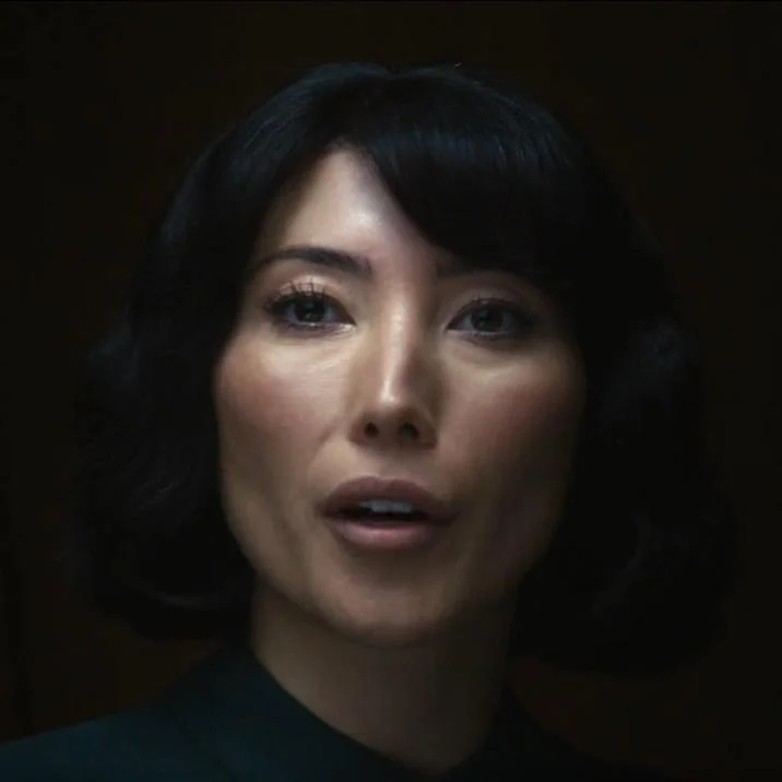 Your Outie Likes X Learning About Your Outie — Close-up of Ms. Casey from Severance speaking softly in a dark room.